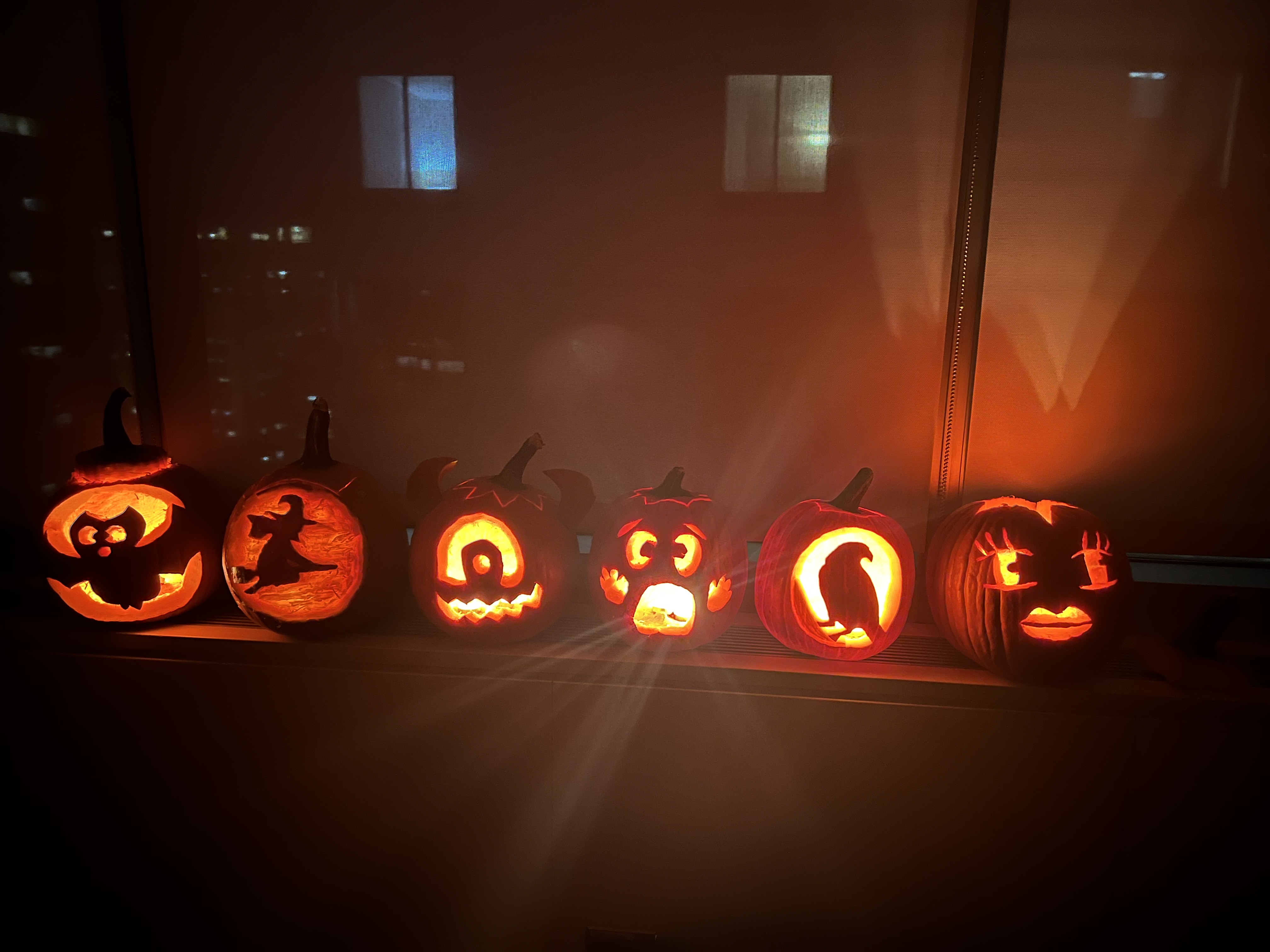 Carved pumpkins lit on a windowsill above the city at night